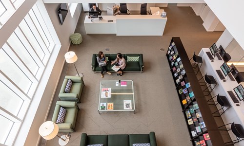 A view of the AKC library from the top of AKC, with people sitting on the reception and sofas utilising the library space 