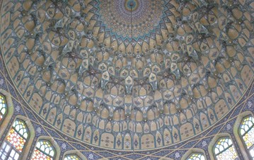 An image from inside of a dome with diverse geometrical patterns in blue shades and windows in a circle with flower mosaic